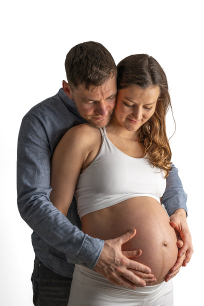 自豪的父母用双手捧着母亲裸露的、圆圆的孕肚，等待着他们的宝宝。孕晚期——第36周。正面视角。白色背景。明亮的照片。图片下载
