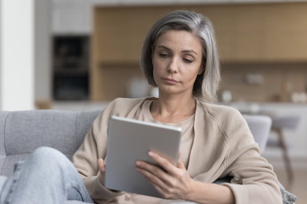 严肃迷人的成熟女人在家里的沙发上拿着平板电脑图片下载