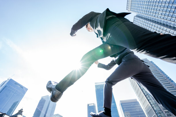 一个商人穿两套西装，经过一个跳跃的城市周围的建筑在蓝天下图片下载