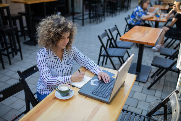 漂亮的年轻女子留着非洲式发型，正在咖啡馆用笔记本电脑工作。图片下载