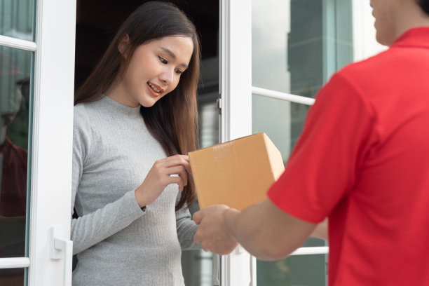 快乐微笑的女人从前门的快递员那里收到盒子包裹。快递员送快递。网购、纸盒、外卖、邮差、快递服务、包裹图片下载