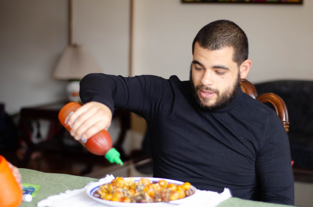 一个人在餐桌上给他的午餐调味。男人准备好吃饭了。即食食品图片下载
