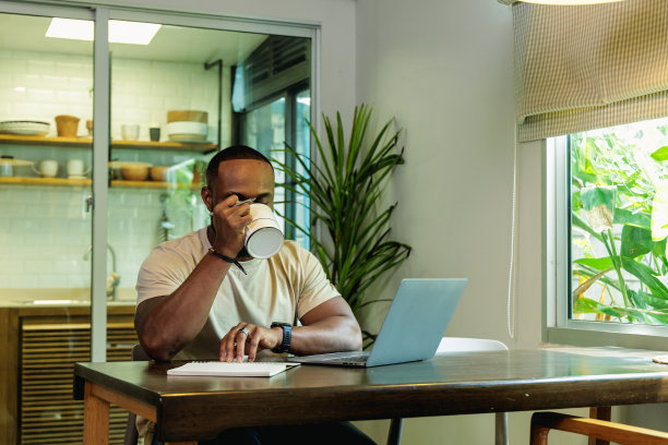 非洲成年男性在家工作，一边喝着热咖啡，一边使用笔记本电脑图片下载