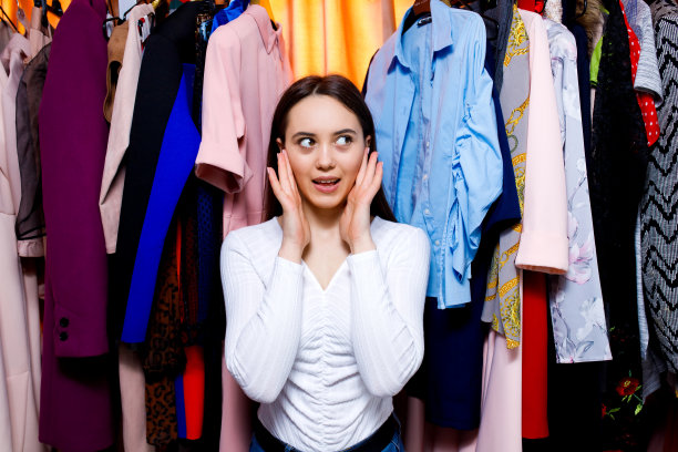 年轻漂亮的十几岁的女孩手牵着手看着可爱的衣服挂在衣架上。图片下载