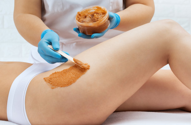 美容师在一个女人的大腿上做美容脱皮手术。美容院的水疗程序。图片下载