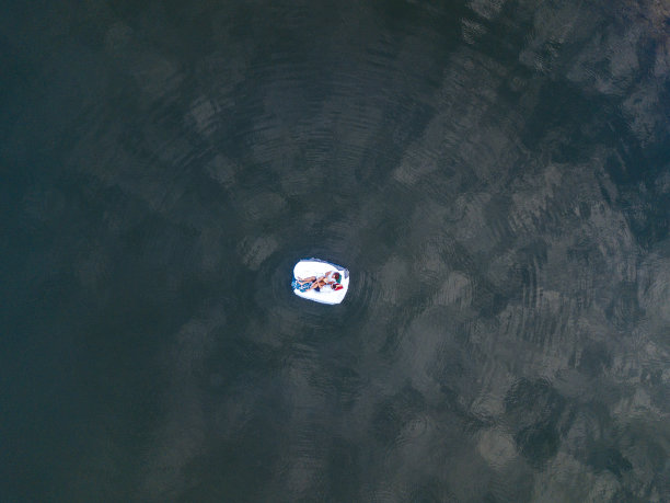 美丽的夫妇睡在床垫上，白色的床上用品漂浮在水面上。无人机视角图片下载