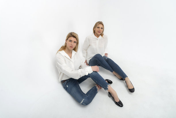 这位穿着白衬衫和蓝色牛仔裤的成熟女人和美丽的照片模特在白色背景的工作室里艺术地摆姿势。图片下载