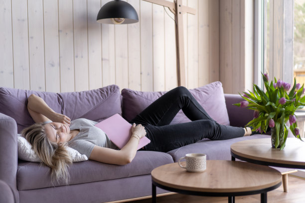 睡眠问题。穿着粉色t恤和牛仔裤的金发美女手里拿着笔记本电脑在家里的沙发上睡着了。在家上网工作。周末。过度劳累。乏力图片下载