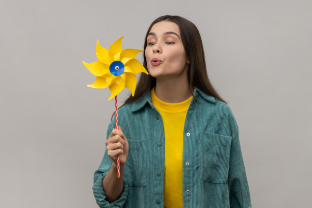 美丽的年轻成年女子吹在纸风车，风车玩具棒。图片下载