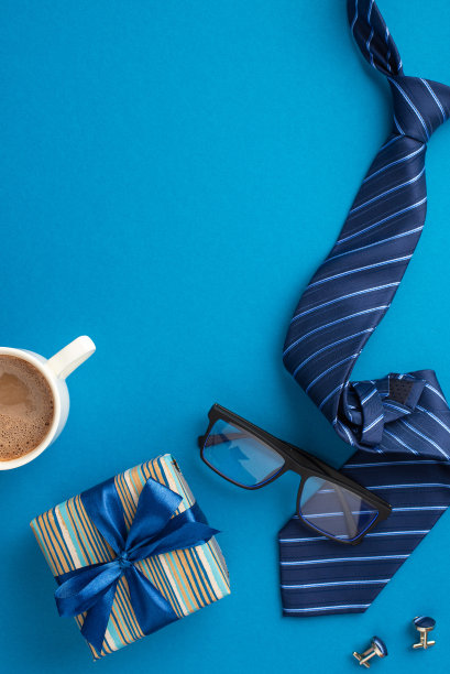 父亲节的概念。俯视图垂直照片的时尚礼品盒丝带蝴蝶结蓝色领带眼镜杯咖啡和袖扣在孤立的蓝色背景图片下载