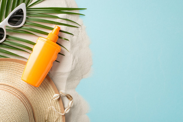 防晒及沙滩用品主题。顶部的SPF霜容器没有品牌，眼镜，遮阳帽，贝壳手镯，棕榈叶在柔和的蓝色和沙质背景与标签的空间图片下载