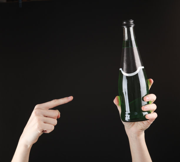 一位女士手持一瓶黑色背景的绿色爱尔兰啤酒图片下载