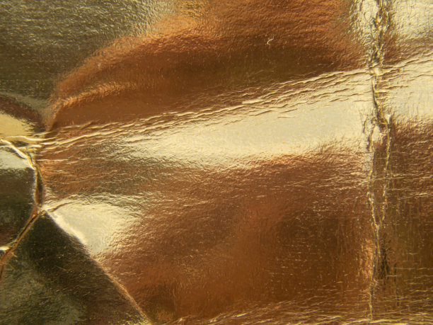 特写金色和皱巴巴的纸，垃圾背景和光反射。图片下载