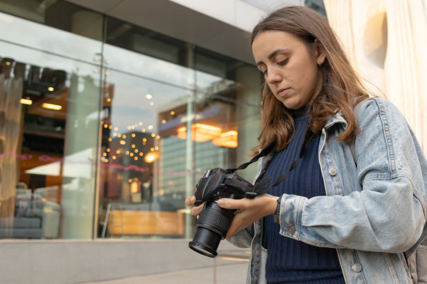 年轻女子专注地看着她的专业相机在模糊的背景灯光。图片下载