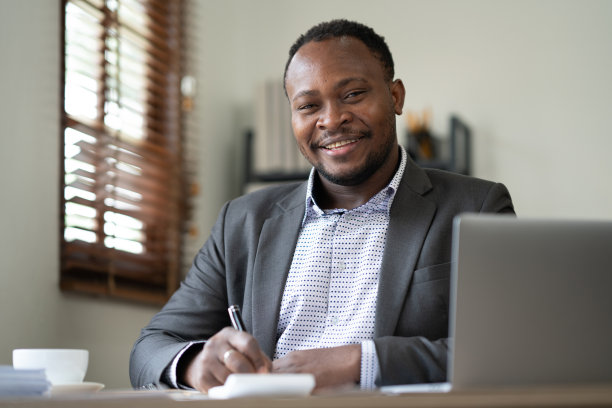 成功商人的肖像，自信地微笑，坐在办公桌前工作图片下载