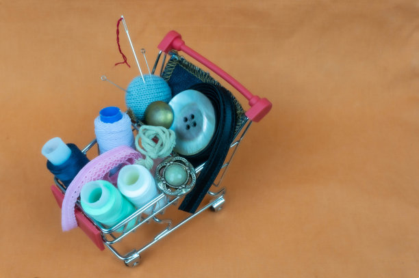 装有线、缝纫配件和纽扣的手推车。背景由淡橙色织物制成。图片下载