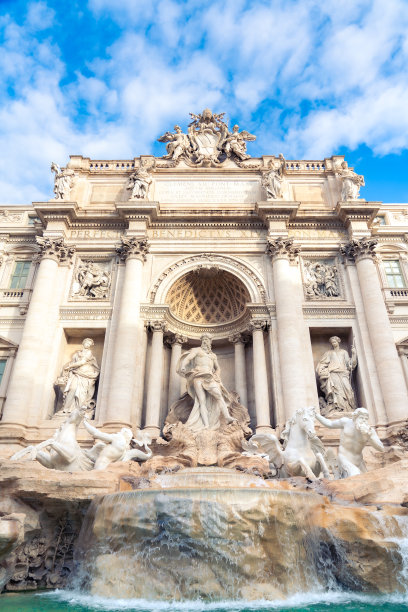 意大利罗马，多云的天空下，清澈的水，旧城的建筑和雕塑，特雷维喷泉的低角度外立面，令人惊叹图片下载