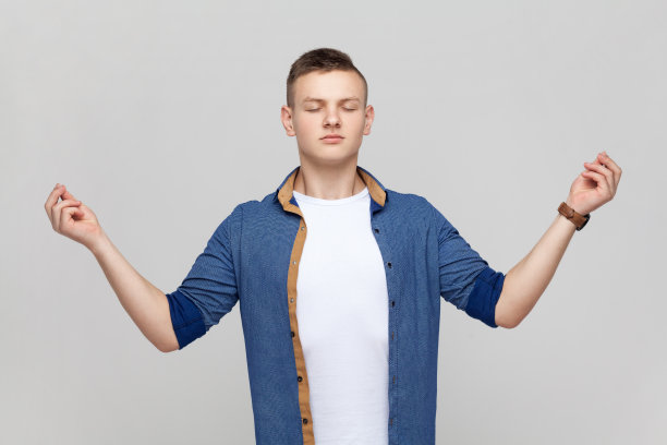 冷静的冥想少年穿着蓝色衬衫，闭着眼睛和瑜伽姿势站着。图片下载