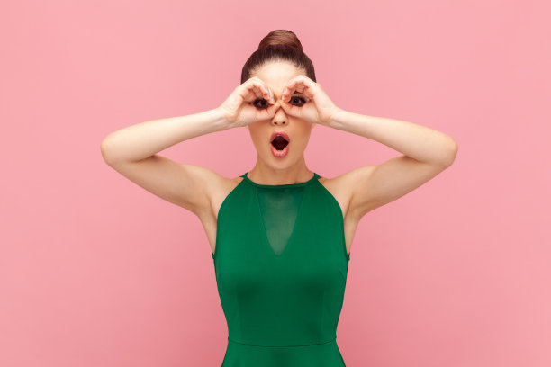 惊讶的女人站在那里用双筒望远镜做手势，张大嘴巴看着，看到了一些惊讶的东西图片下载