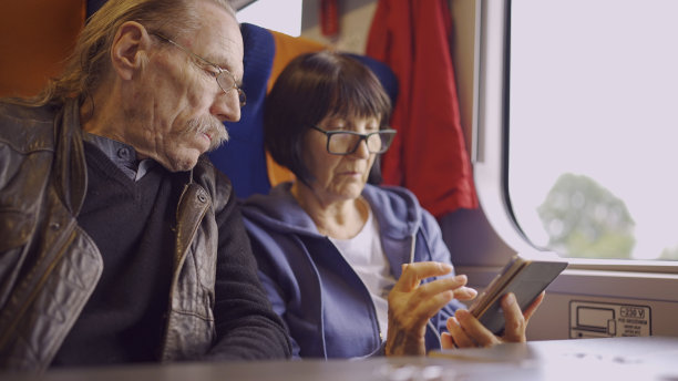 老夫妇乘火车旅行，女士手里拿着手机，两人都在看智能手机，互相交谈图片下载