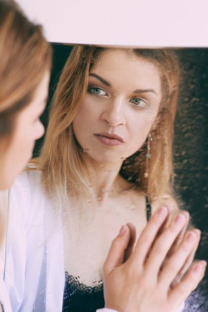 穿着白衬衫的金发美女站在镜子旁边。医疗保健美容心理问题图片下载