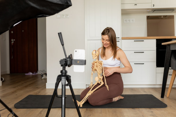 年轻女博主的肖像坐在地板上，指着瘦弱的手，解释，用智能手机拍摄视频。图片下载
