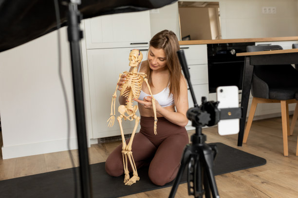 年轻漂亮苗条的女人手持骨架，指着肋骨，用智能手机拍摄视频。图片下载