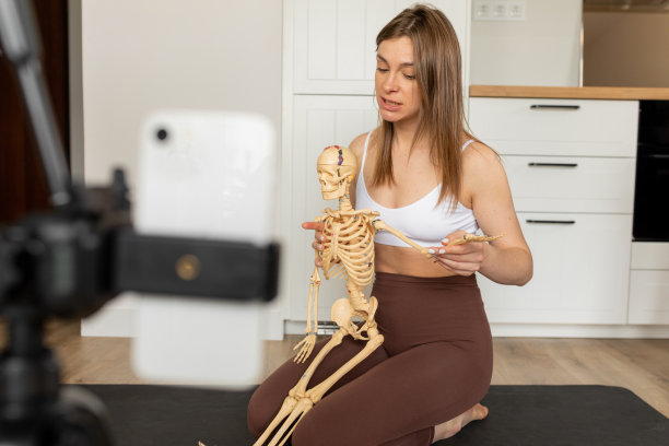 年轻苗条的女博主的肖像坐在那里，拿着瘦骨嶙峋的手，一边解释，一边用智能手机拍摄视频。图片下载