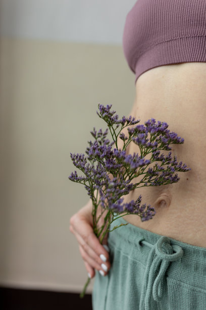一张被剪裁过的照片，年轻苗条的女人裸露着肚子，拿着一束盛开的紫色薰衣草，摆姿势。图片下载