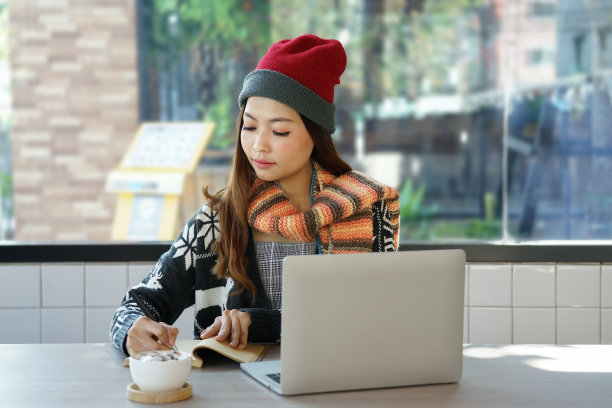 一名亚洲妇女穿着冬装，带着笔记本电脑在咖啡店里随意工作图片下载