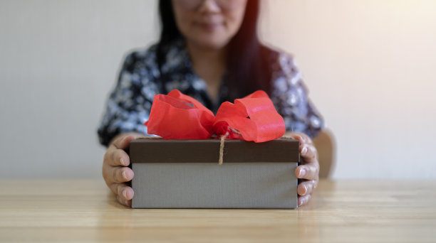 选择性的聚焦在礼盒上，女性的手拿着木桌上的红丝带礼盒的镜头。图片下载