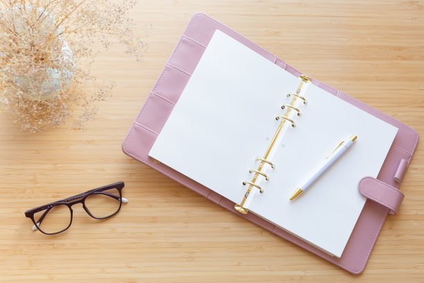 平铺，顶部的一个粉彩粉红色规划师，干花束，玻璃和文具在一个木制的表面。图片下载