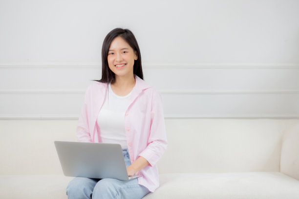 年轻的亚洲商业女性在家里用笔记本电脑在客厅的沙发上上网，自由职业者女孩坐在沙发上用笔记本电脑舒适放松，生活方式的概念。图片下载