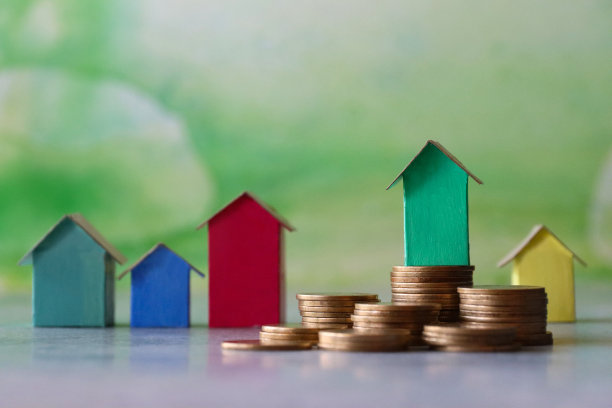 近距离图像成堆的硬币在一排排彩色纸板房子，彩色的海滩小屋，重点在前景，斑斑驳杂的绿色背景，家庭财务，房地产和假日储蓄概念图片下载