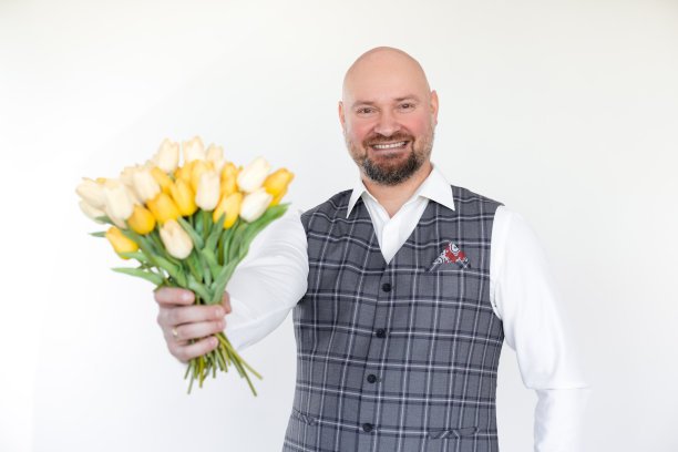 微笑的中年商人的肖像，身穿灰色背心，白色衬衫持有，赠送黄色郁金香花束。假期。图片下载