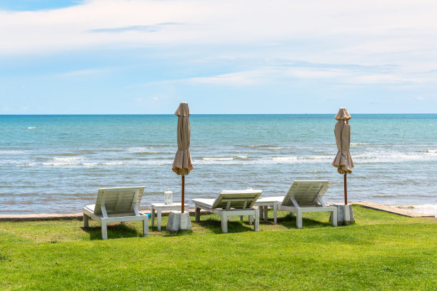 木制太阳躺椅与封闭的阳伞和凉亭在绿色的草坪在热带的海洋和蓝色的天空图片下载