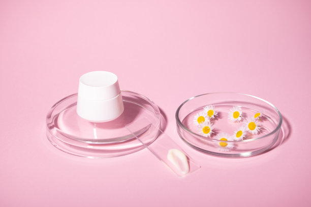 静物白色模型罐，培养皿中的洋甘菊和实验室玻璃上的保湿霜，在粉红色的背景上隔离图片下载