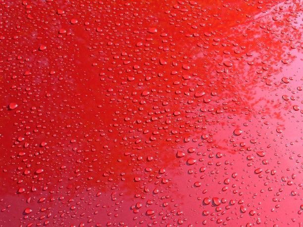 一阵短暂的大雨过后，雨水落在一辆锃亮的红色车身上，在早晨的阳光下闪闪发光。图片下载
