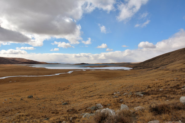 一条浅河蜿蜒的河床，穿过秋天的山谷，流入一个大湖，被初冰包围，被高山环绕。图片下载