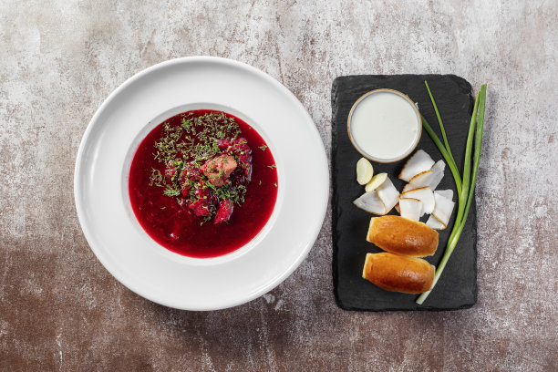 乌克兰罗宋汤配大蒜甜甜圈、大葱和培根，旁边是一碗酸奶油。汤被倒进一个轻陶瓷盘子里。盘子放在浅色的背景上。图片下载