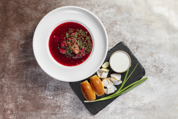 乌克兰罗宋汤配大蒜甜甜圈、大葱和培根，旁边是一碗酸奶油。汤被倒进一个轻陶瓷盘子里。盘子放在浅色的背景上。图片下载