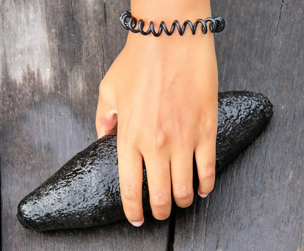 一张照片上，一个女人的手戴着一个黑色的手镯，有人拿着一个黑色的东西放在木桌上图片下载