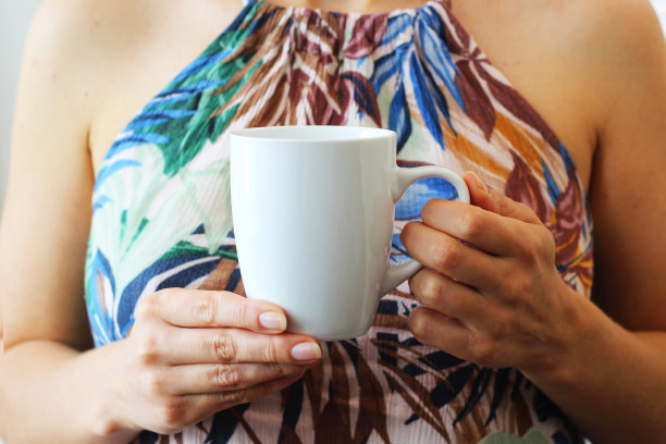 拿着白色咖啡杯模型的女孩。空白的白色杯子模拟你的公司标志和设计。图片下载