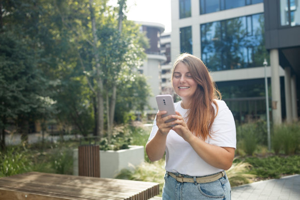 肖像微笑着年轻的高加索美女在城市外看手机图片下载