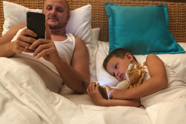拍摄一对父子晚上在床上使用智能手机。图片下载