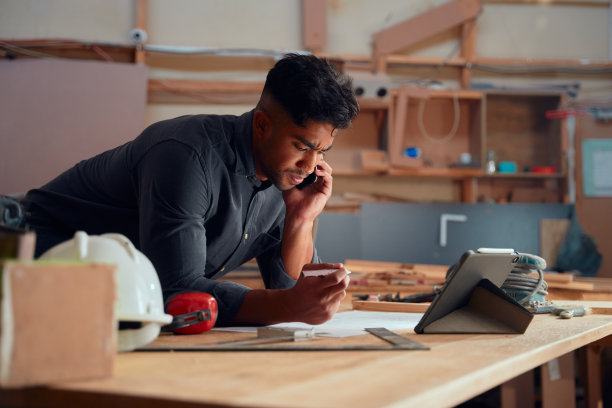 木工工厂里，一名专注于手机的年轻人靠在数码平板电脑旁图片下载