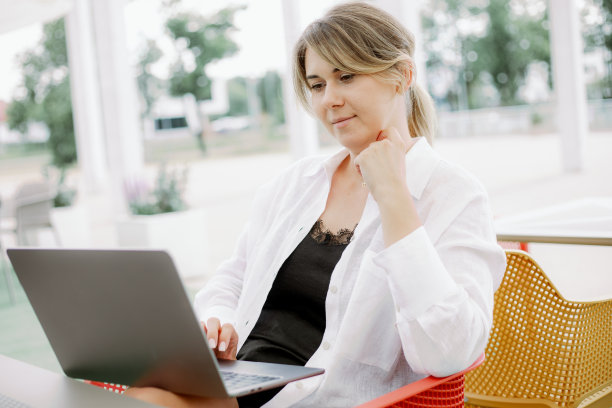 自由职业者喜欢坐在户外咖啡馆的椅子上用笔记本电脑工作。女人摸着脖子，看着屏幕。图片下载