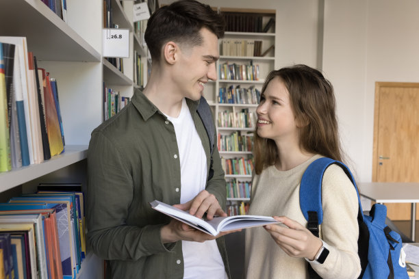 在图书馆里拿着教科书微笑的女孩和男同学图片下载