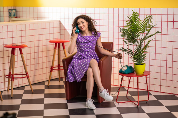 带着灿烂的微笑，一个非常迷人的女人，穿着平裙，坐在复古咖啡馆的沙发上，她用老式的电话和别人聊天图片下载