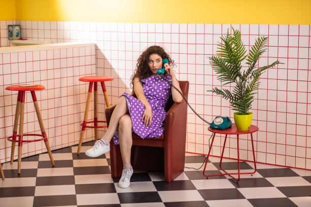 在复古的咖啡馆里，一位快乐而兴奋的女士坐在沙发上，用老式的家庭电话和别人讨论着什么图片下载